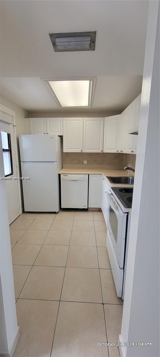 Kitchen featuring white cabinetry, solid-surface countertops, tile flooring, and integrated white appliances