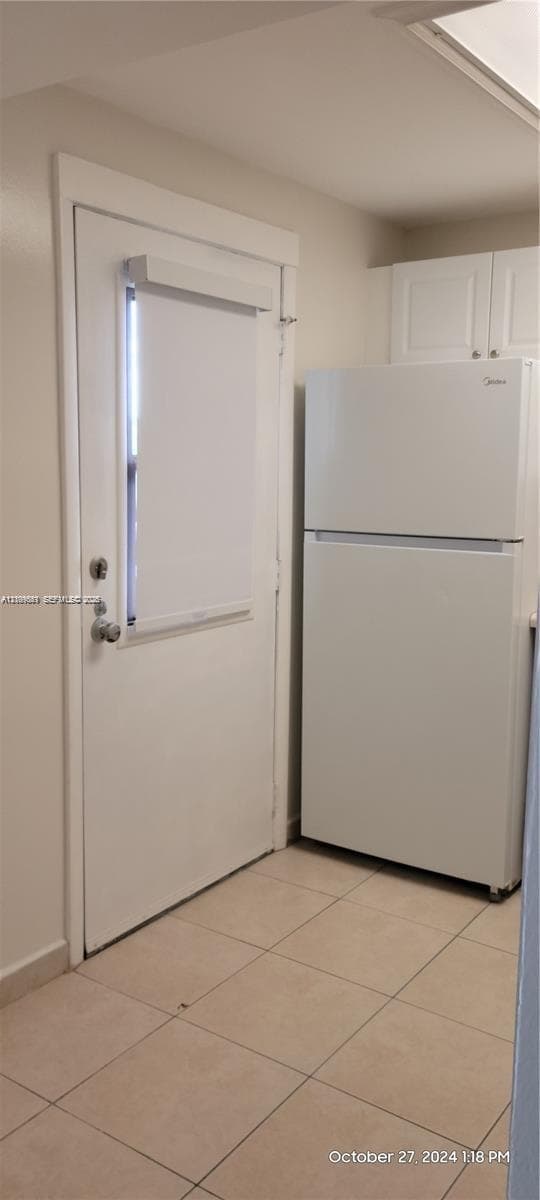 White top-mount refrigerator, neutral ceramic tile flooring, and exterior door with a vertical window insert