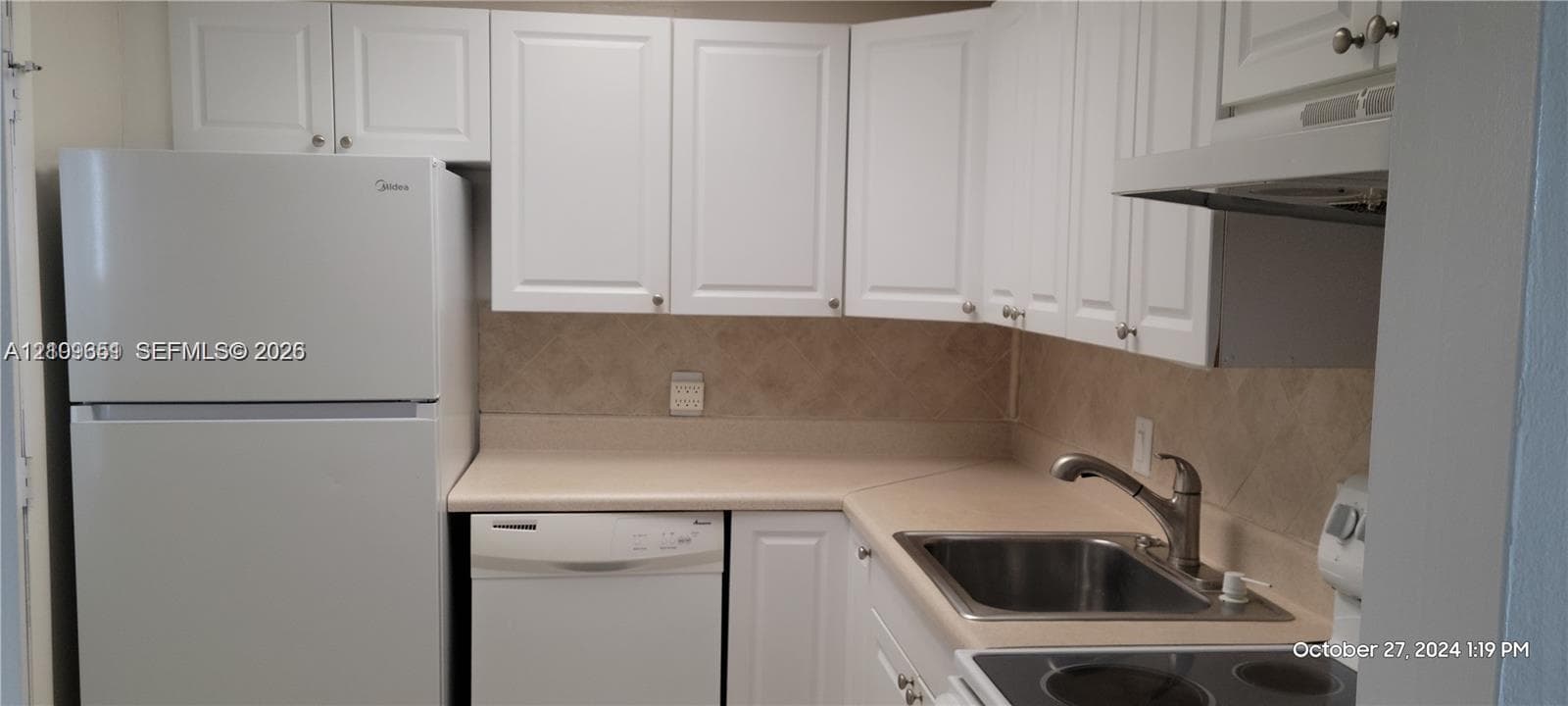 Kitchen featuring white shaker-style cabinetry, solid-surface countertops, a tiled backsplash, a stainless steel sink with a high-arch faucet, and an integrated range hood