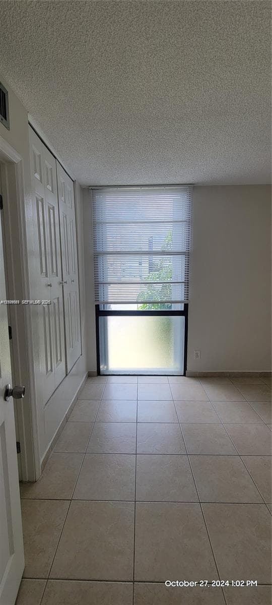 Neutral-toned tile flooring, floor-to-ceiling window with white roman shades, and built-in closet storage with paneled doors