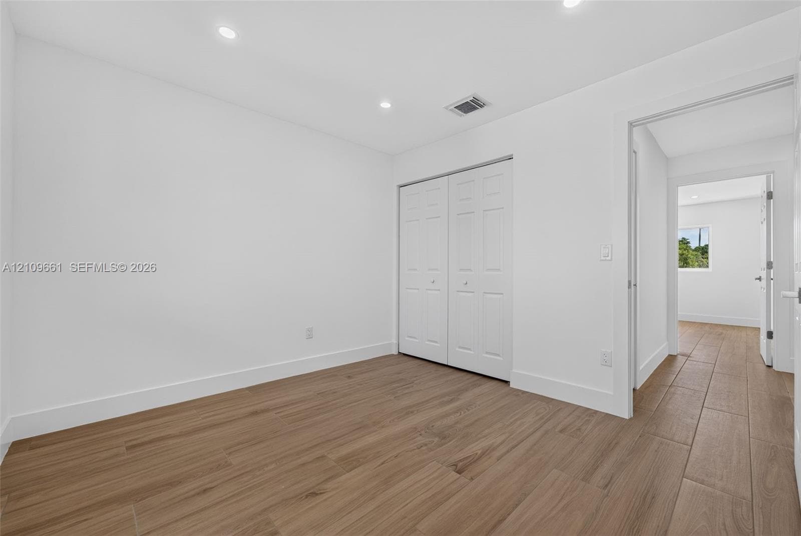 Neutral interior featuring wood-finish tile flooring, recessed ceiling lighting, and a double-door closet with paneled detailing