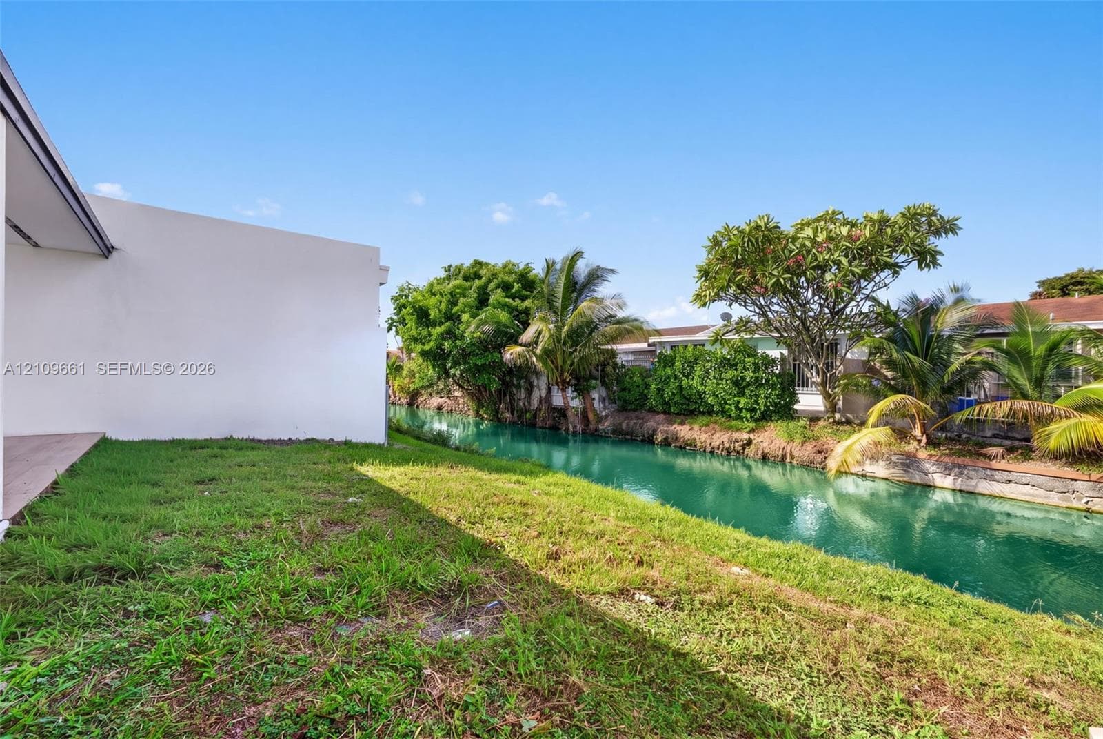 Waterfront exterior featuring a grassy lawn, canal access, and mature landscaping