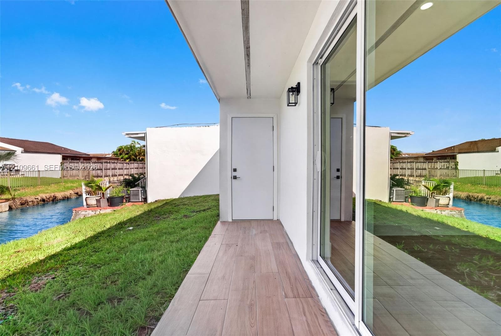 Covered patio featuring wood-finish tile flooring, sliding glass doors, and a solid exterior door, situated along a water feature