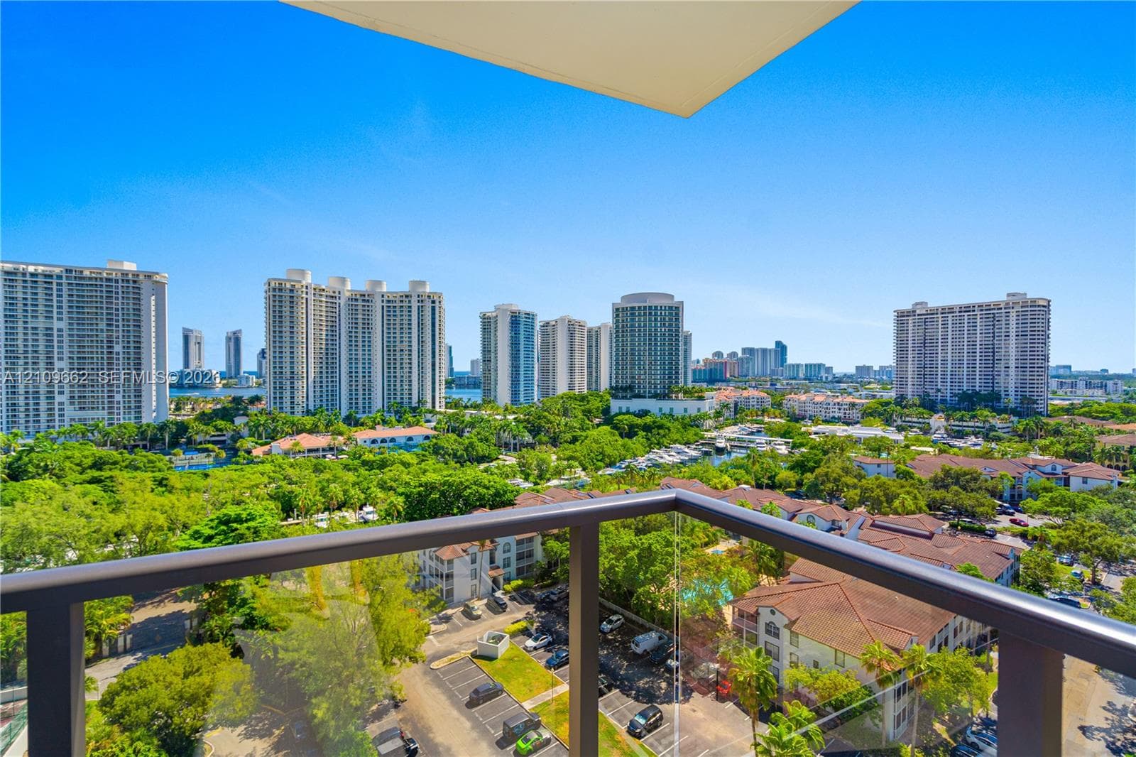 Private balcony featuring a metal frame and glass railing overlooking a cityscape and lush greenery