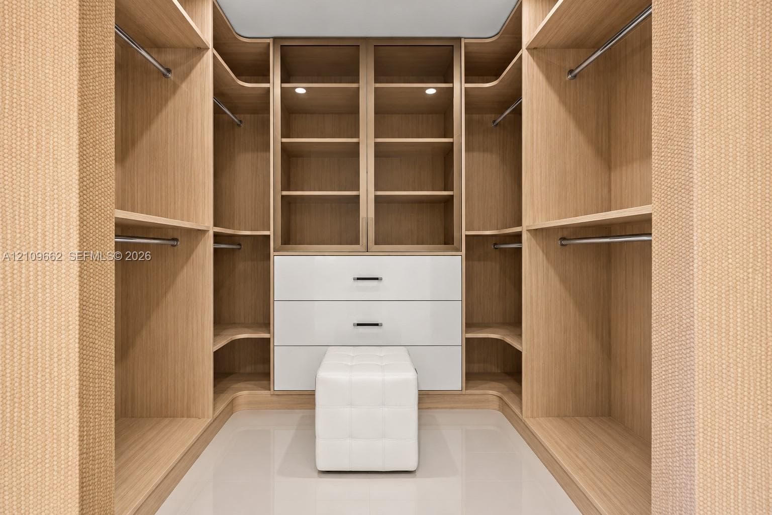 Custom closet featuring built-in wood-finish cabinetry, floor-to-ceiling shelving, integrated garment rods, and a white lacquer three-drawer storage unit