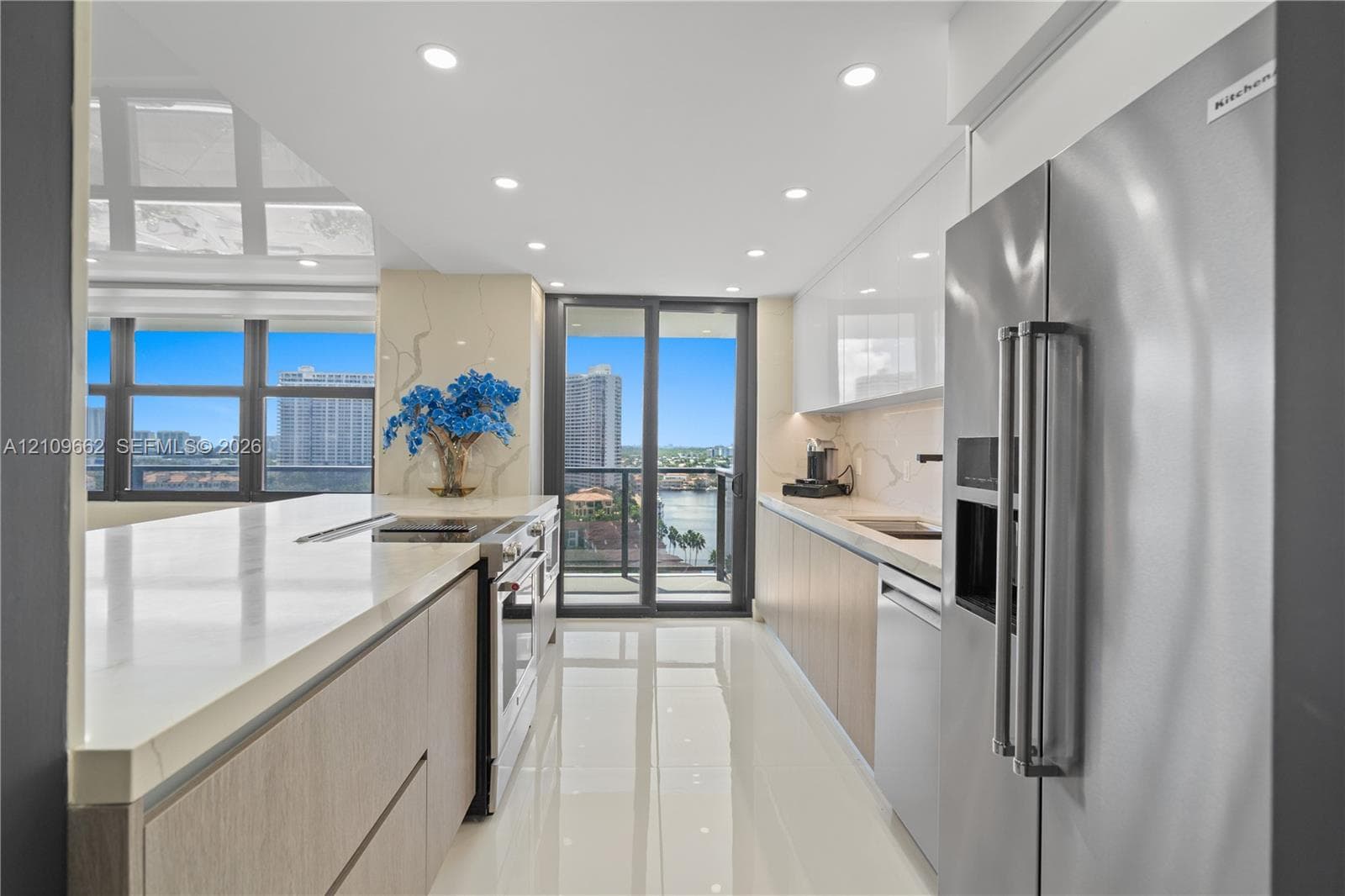 Modern kitchen featuring flat-panel cabinetry, light-toned stone countertops, integrated stainless steel appliances, recessed ceiling lighting, and polished large-format tile flooring