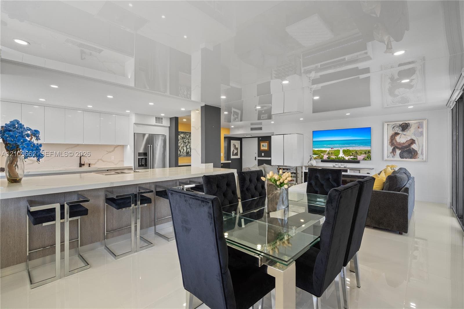 Modern kitchen featuring sleek white cabinetry, a sprawling center island with stone-finish countertops, recessed lighting, and high-gloss reflective ceiling surfaces