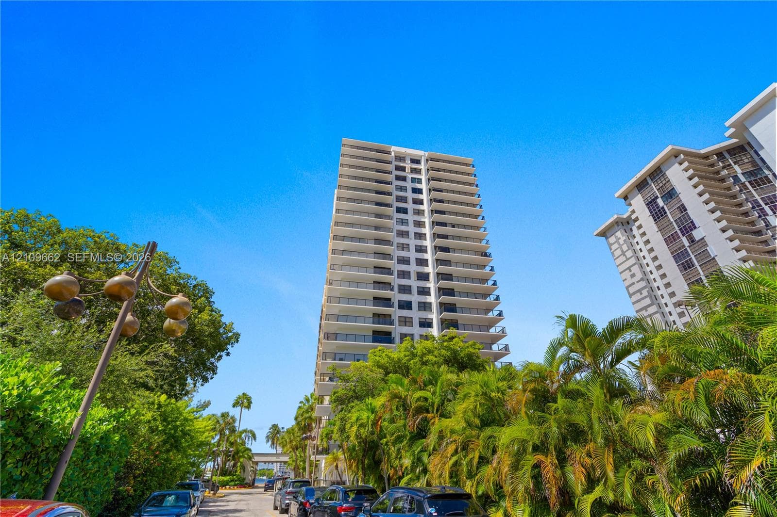 High-rise residential building featuring private balconies, expansive windows, and mature tropical landscaping