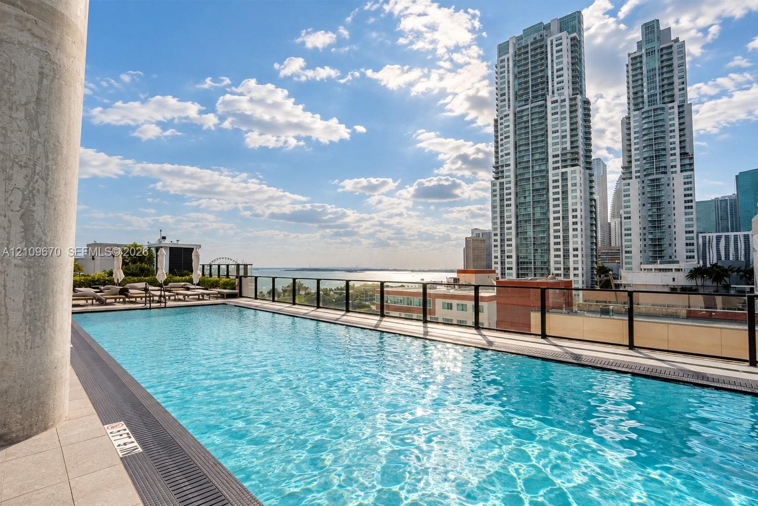 Rooftop swimming pool featuring a tile perimeter, black metal railings, and a backdrop of urban high-rise buildings and water