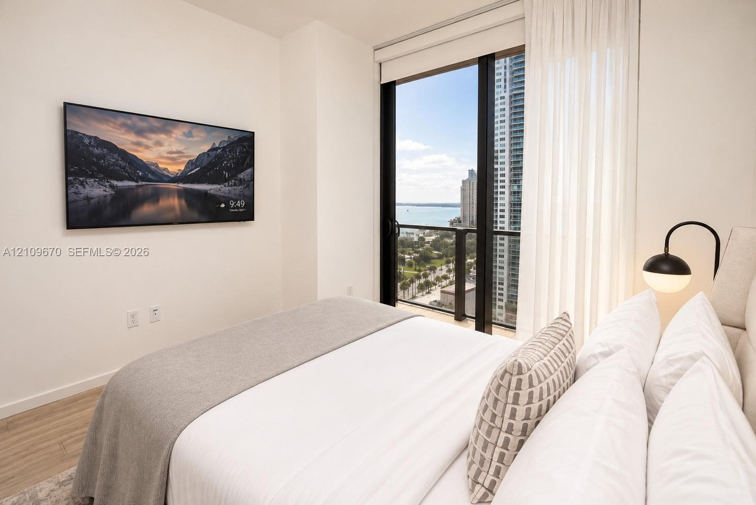 Floor-to-ceiling sliding glass door, wood-finish flooring, and expansive exterior city and water scenery