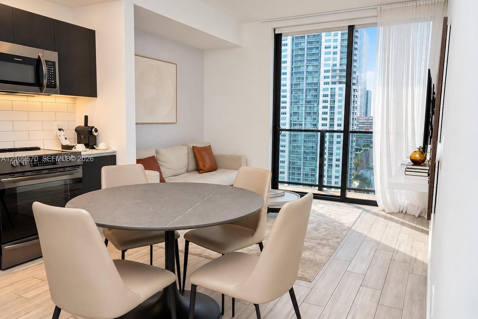 Kitchen featuring matte black cabinetry, stainless steel appliances, and a subway tile backsplash, complemented by wood-finish flooring and floor-to-ceiling windows with balcony access