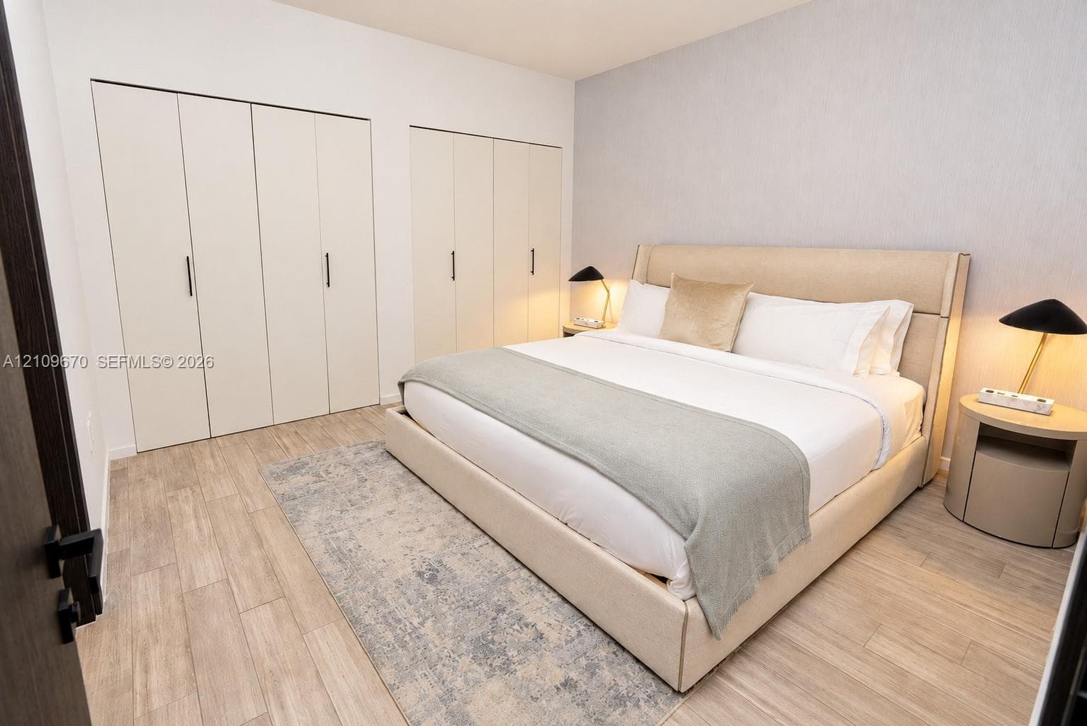 Bedroom featuring wood-finish flooring, dual built-in closets with vertical hardware, and a neutral-toned accent wall