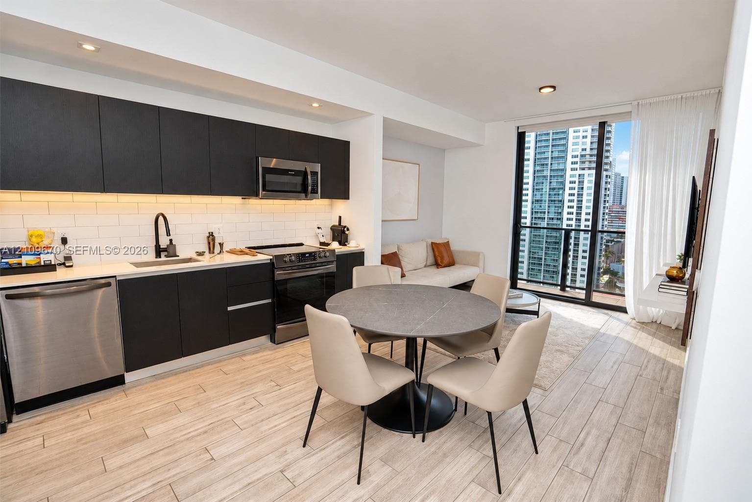 Kitchen featuring matte black cabinetry, stainless steel appliances, white subway tile backsplash, and wood-finish flooring, with floor-to-ceiling windows leading to a balcony