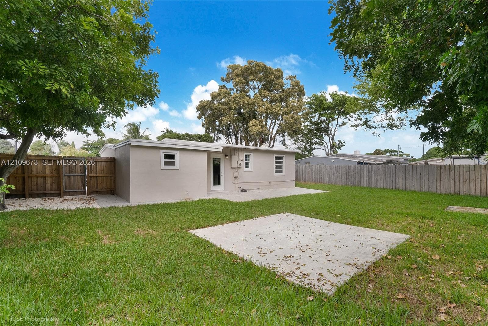 Rear exterior featuring a concrete patio, grassy yard, and wood privacy fencing
