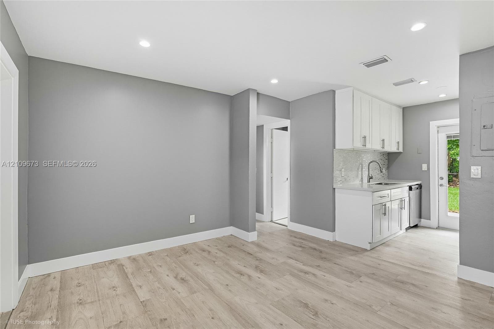 Kitchenette featuring white cabinetry, stone-finish countertops, tile backsplash, and wood-finish flooring