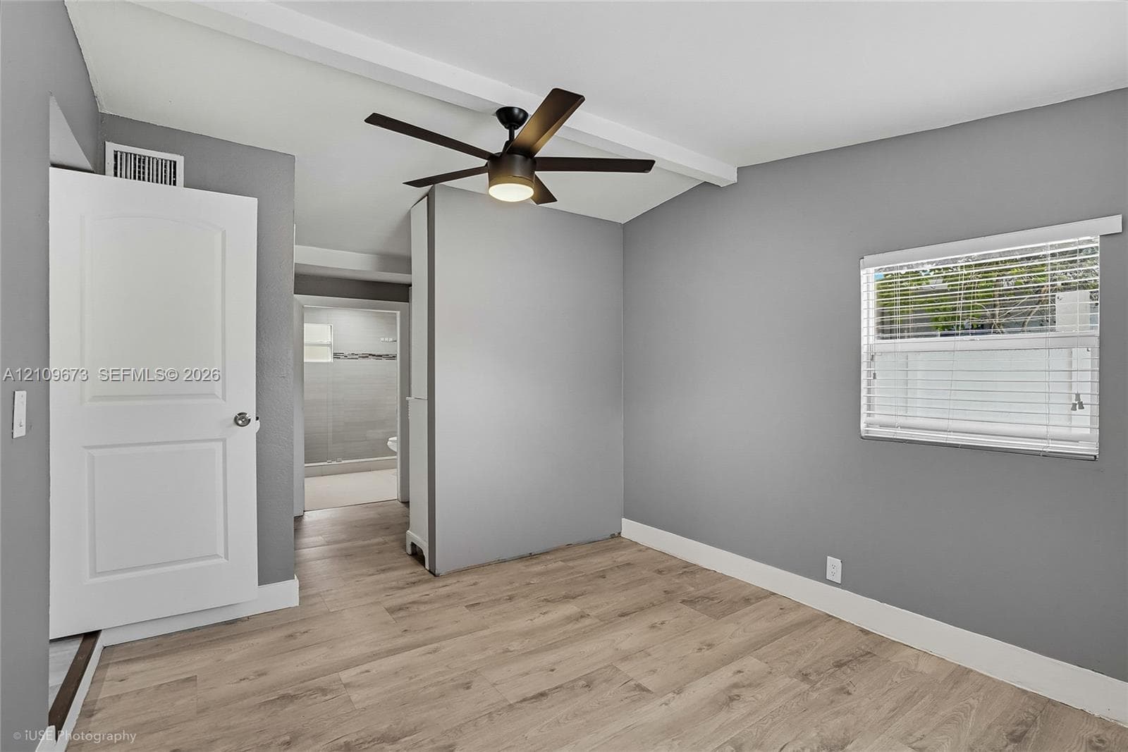 Interior space featuring wood-finish flooring, neutral-toned walls, a white multi-panel interior door, and a ceiling fan with integrated lighting