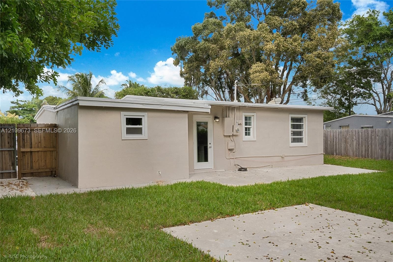 Exterior rear elevation featuring a concrete patio, stucco siding, multi-lite windows, and a wood privacy fence