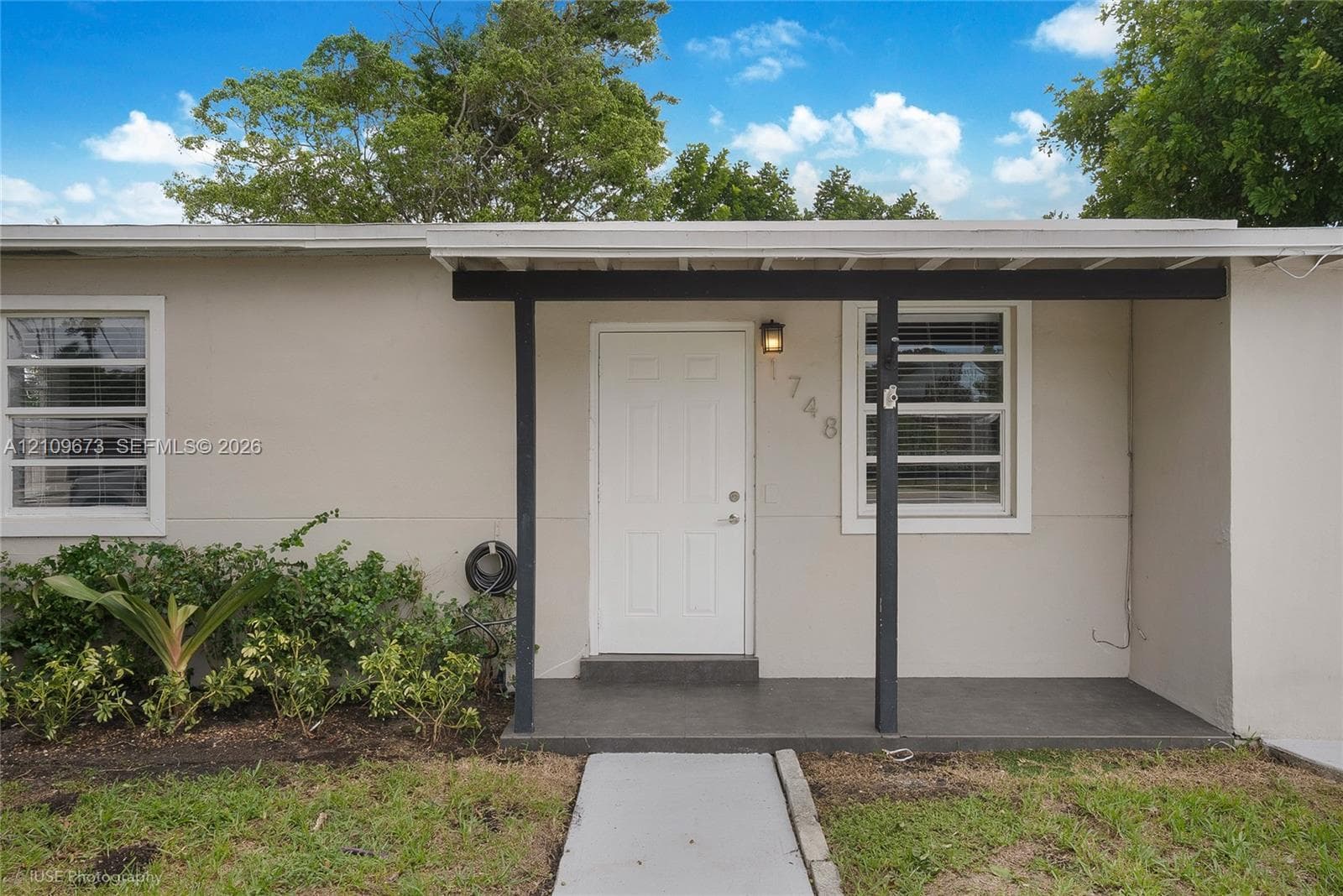 Exterior façade featuring neutral stucco siding, a covered entryway with a concrete porch, and horizontal multi-pane windows