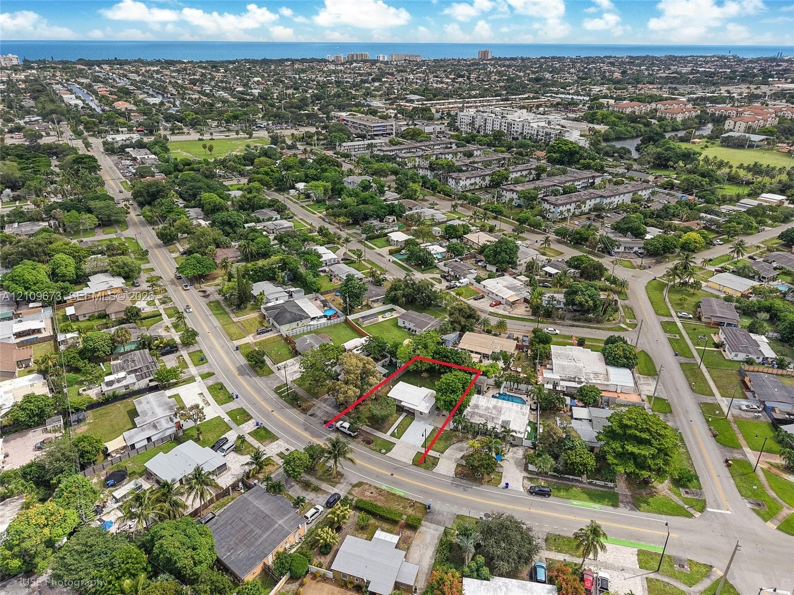 Aerial perspective of a residential lot featuring a detached structure, concrete driveway, mature canopy trees, and established landscaping