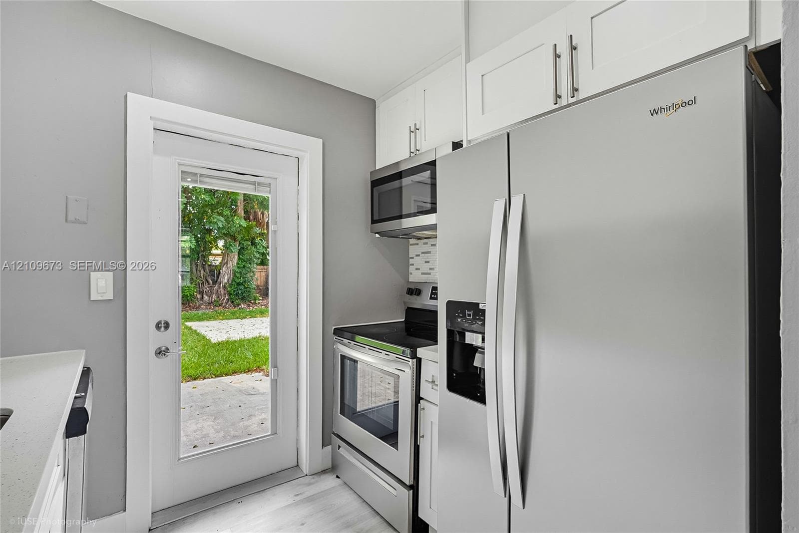 Kitchen area featuring white shaker-style cabinetry, stainless steel appliances, light-toned wood-finish flooring, and a glass-paneled exterior door