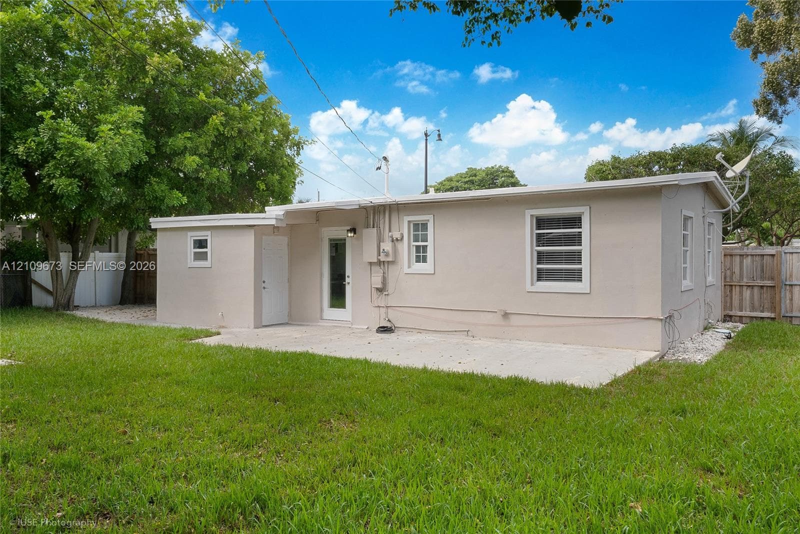 Stucco exterior residence featuring a concrete patio, multi-pane windows, and a fenced backyard with mature trees