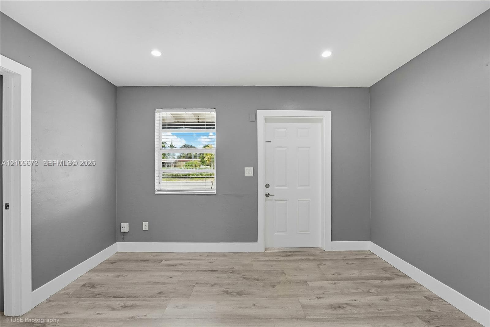 Interior space featuring wood-finish flooring, neutral gray walls, recessed lighting, and a six-panel door