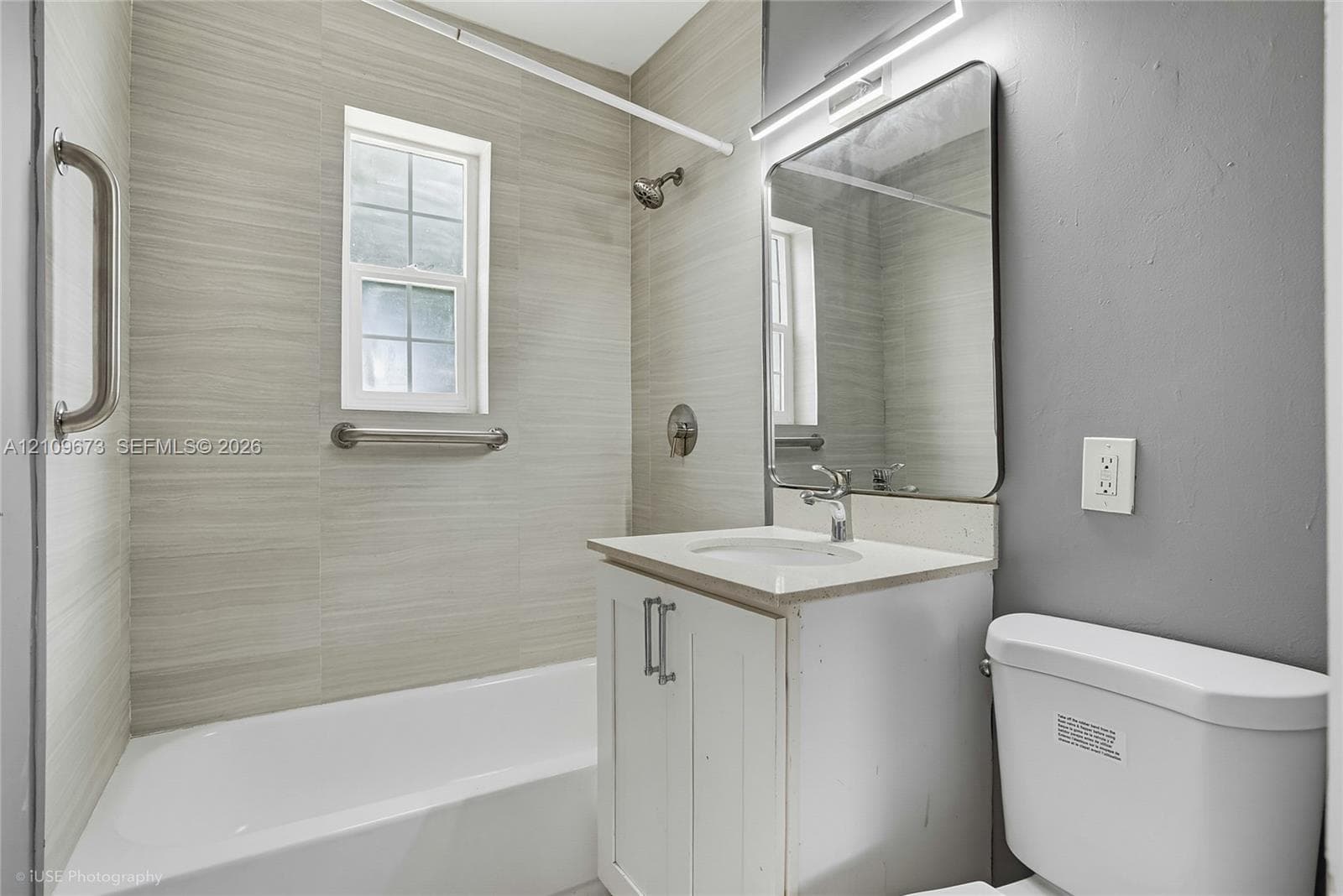 Bathroom featuring a tub-shower combination with horizontal tile surround, white vanity with an integrated countertop, wall-mounted rectangular mirror, and chrome finish fixtures