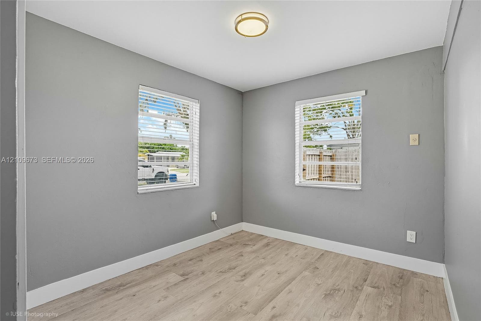 Neutral-toned interior featuring wood-finish flooring, dual windows with blinds, and a flush-mount circular ceiling light fixture