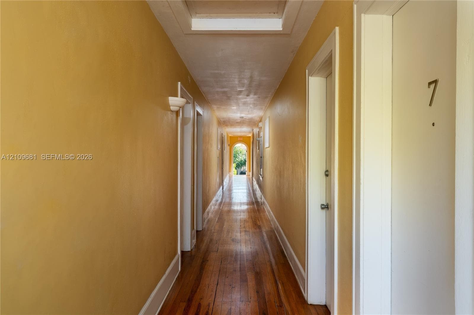 Hallway featuring wood-finish flooring, wall-mounted sconce lighting, and an arched doorway