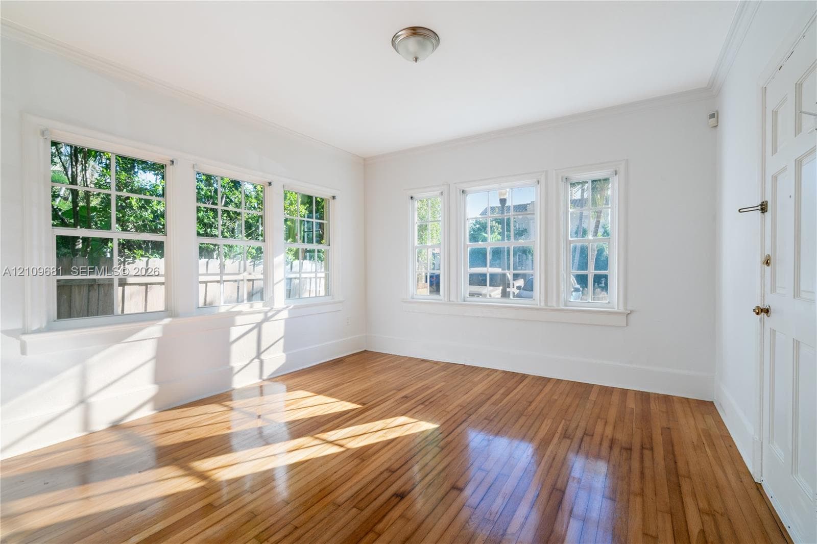 Interior space featuring wood-finish flooring, multi-pane windows, crown molding, and a paneled entry door