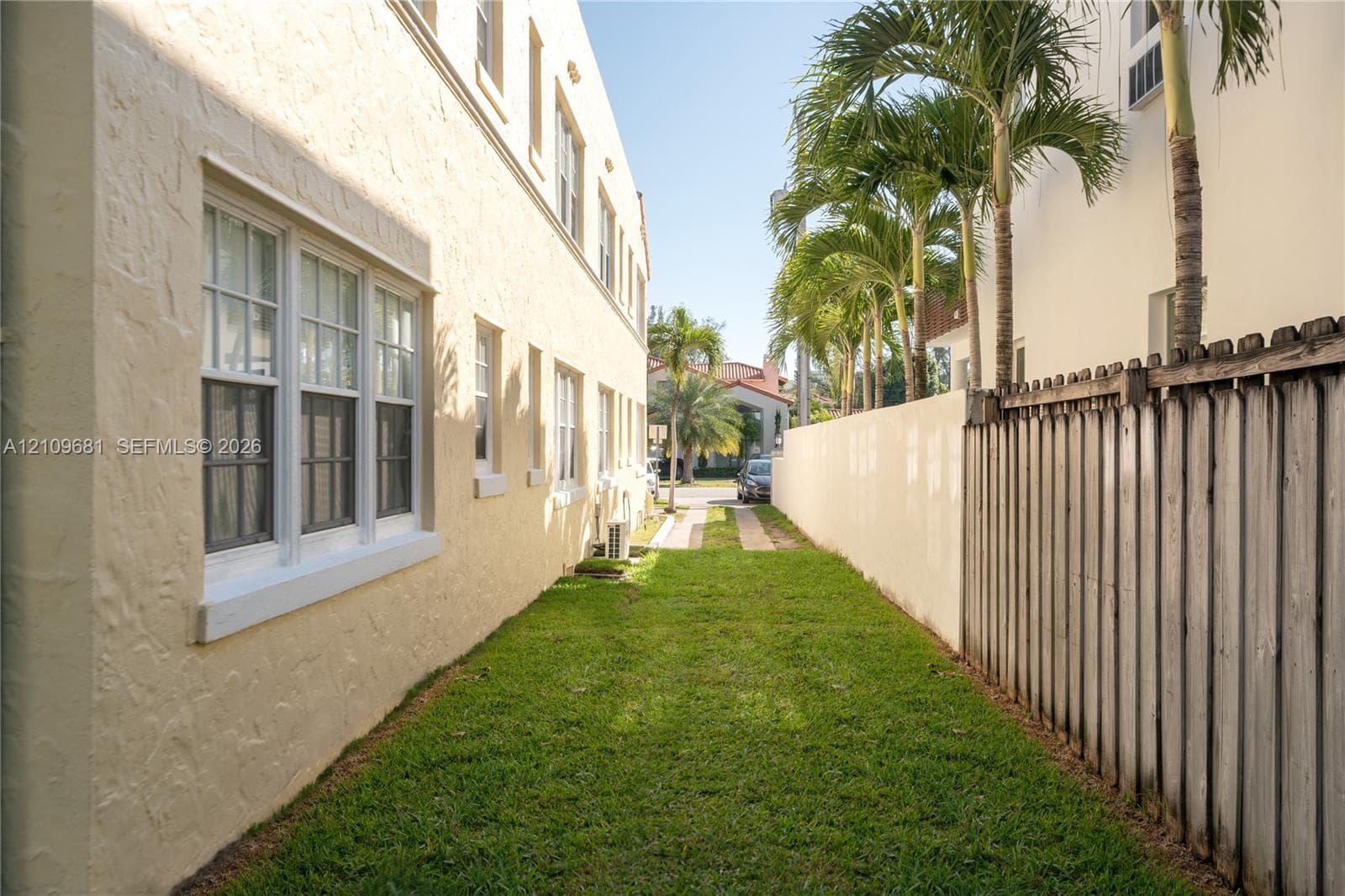 Stucco exterior featuring multi-pane windows, a grass side yard, and mature palm trees