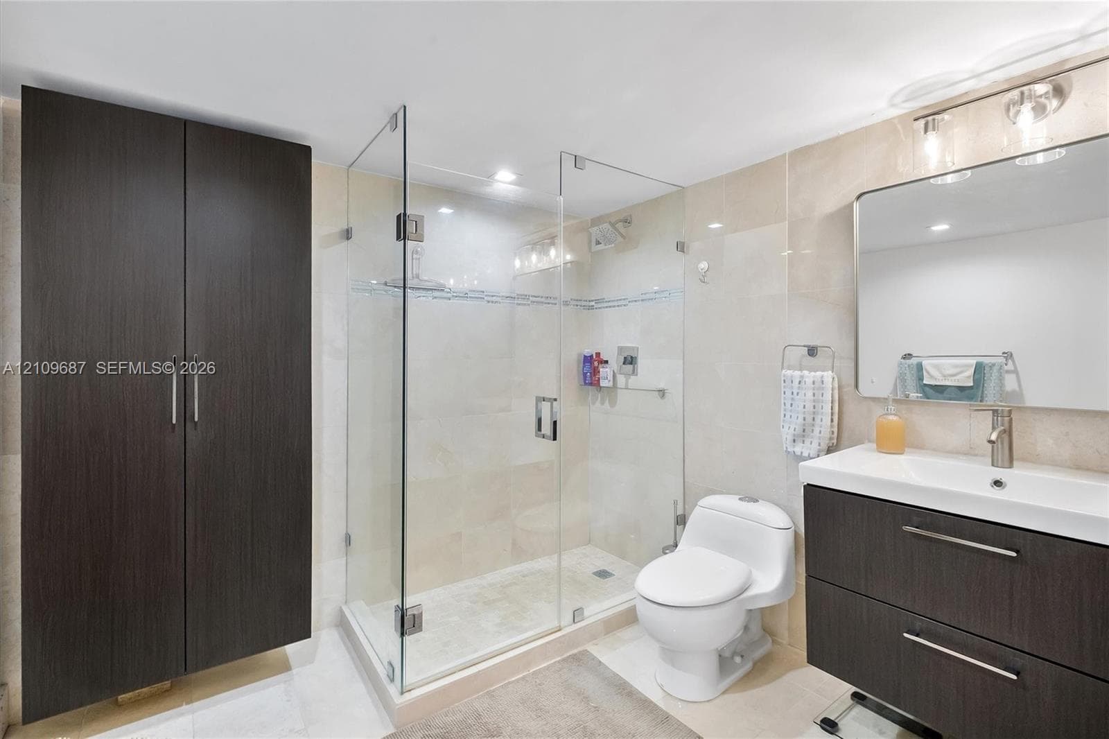 Bathroom featuring a glass-enclosed shower, dark wood-finish cabinetry, a rectangular vanity sink with a metallic faucet, and stone-tile walls