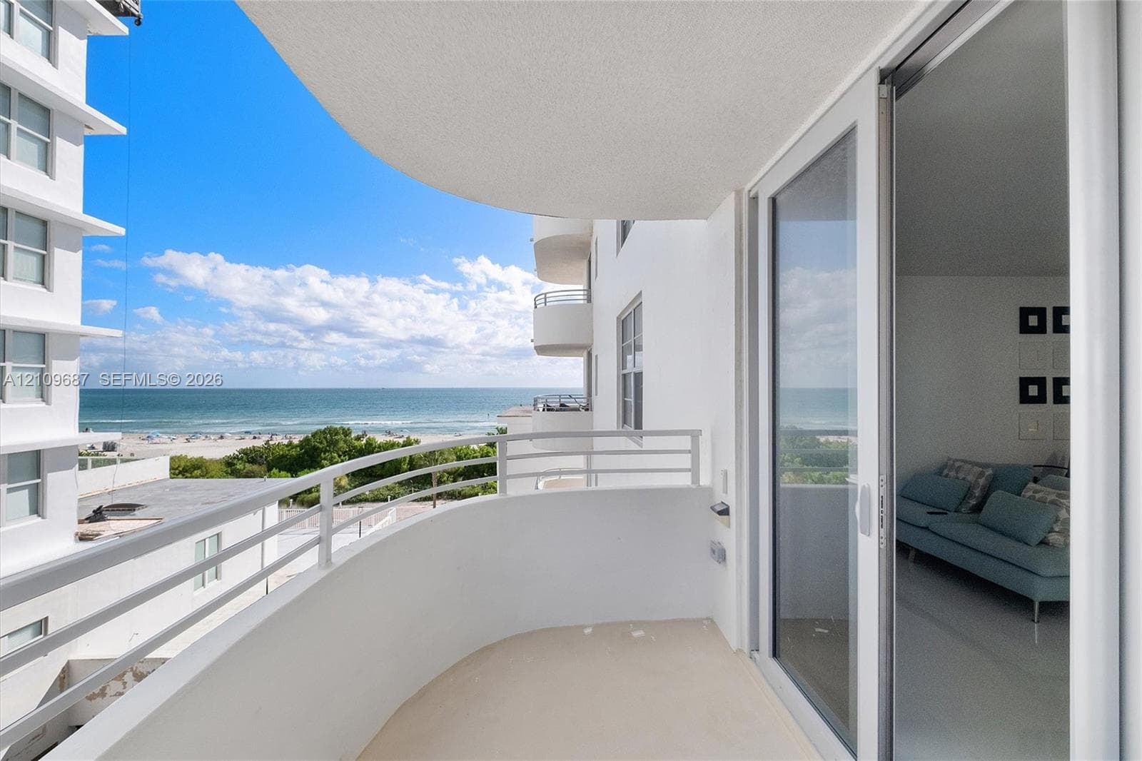 Curved balcony featuring white solid-wall construction, horizontal metal railings, and sliding glass door entry