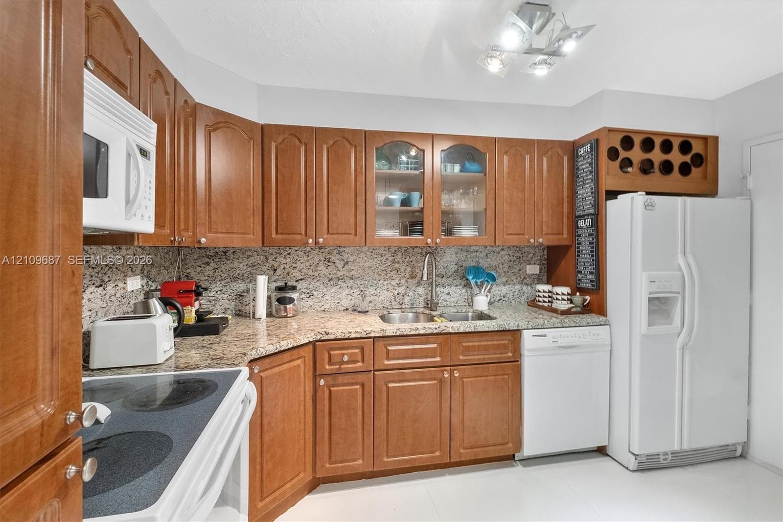 Kitchen featuring wood cabinetry, stone countertops, glass-front upper cabinet doors, built-in wine storage, and a stainless steel double-basin sink