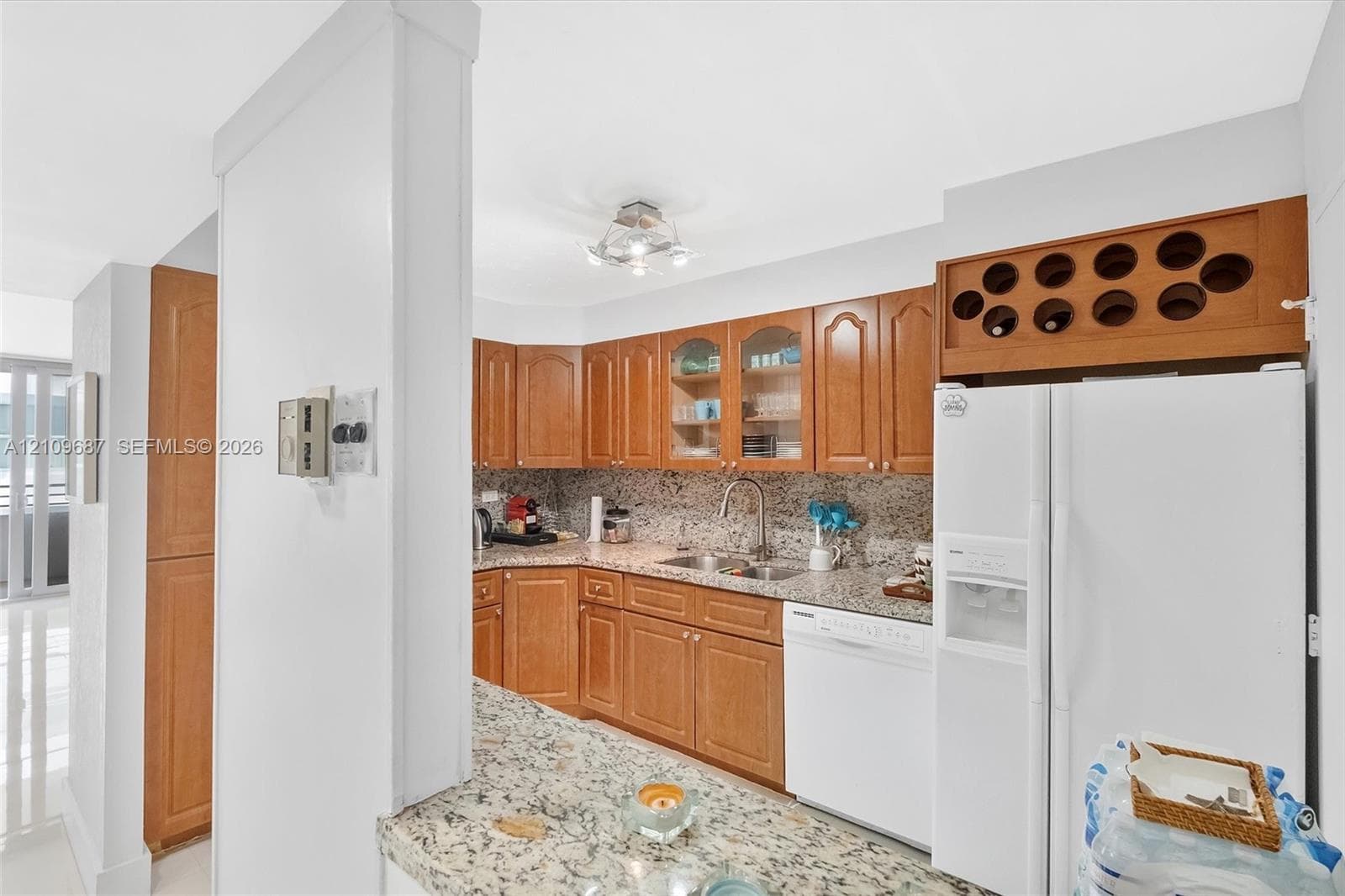Kitchen featuring wood cabinetry, stone-surface countertops, built-in wine storage, a stainless steel sink with a high-arch faucet, and an integrated dishwasher