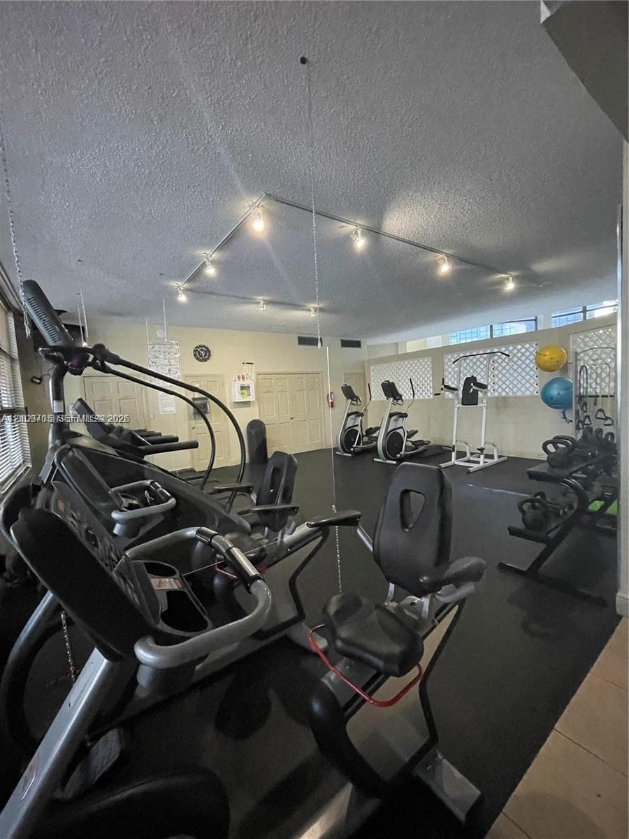 Fitness space featuring rubberized flooring, mounted track lighting, and mirrored wall panels