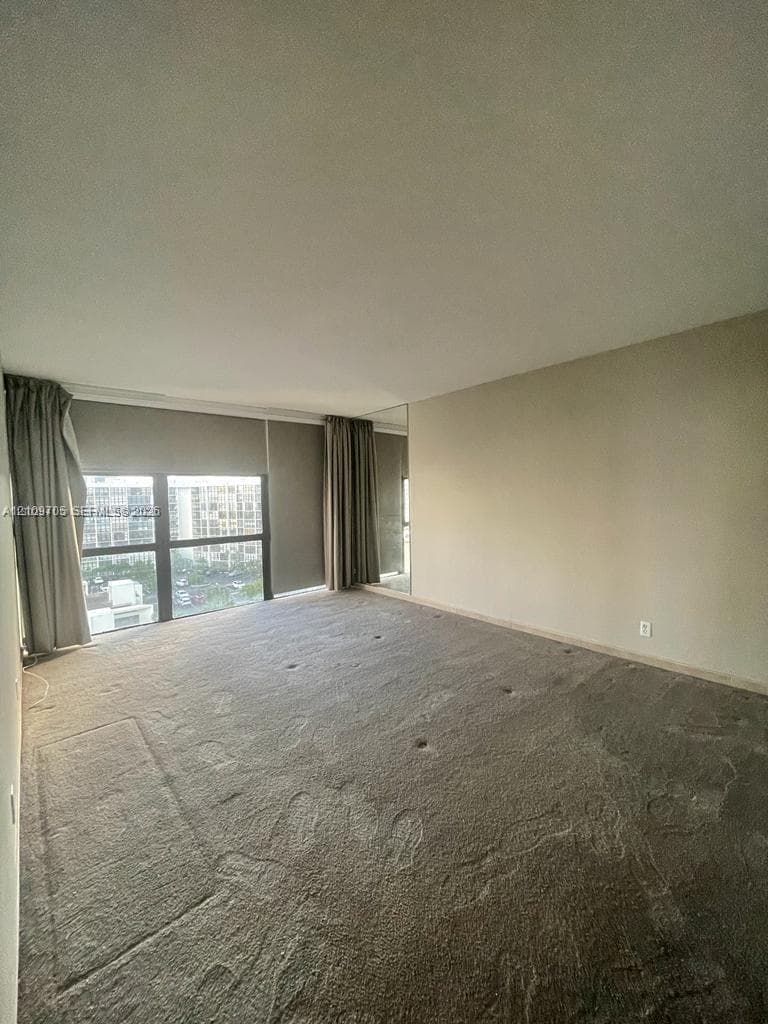Expansive room featuring wall-to-wall carpeting, floor-to-ceiling windows, and a full-height mirrored wall