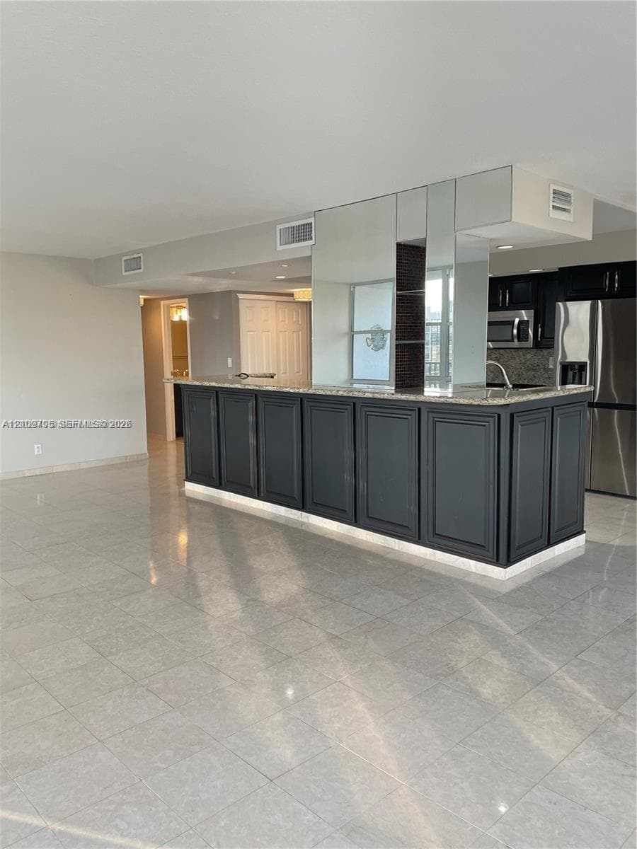 Kitchen featuring a dark cabinetry peninsula with an integrated countertop, reflective wall paneling, tile flooring, and stainless steel appliances