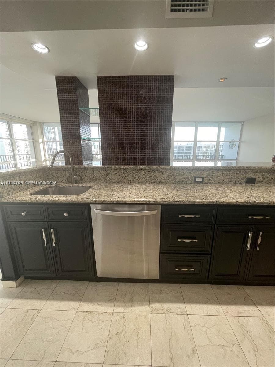 Kitchen featuring dark cabinetry, stone-surface countertops, integrated stainless steel dishwasher, undermount sink with a gooseneck faucet, and mosaic tile backsplash