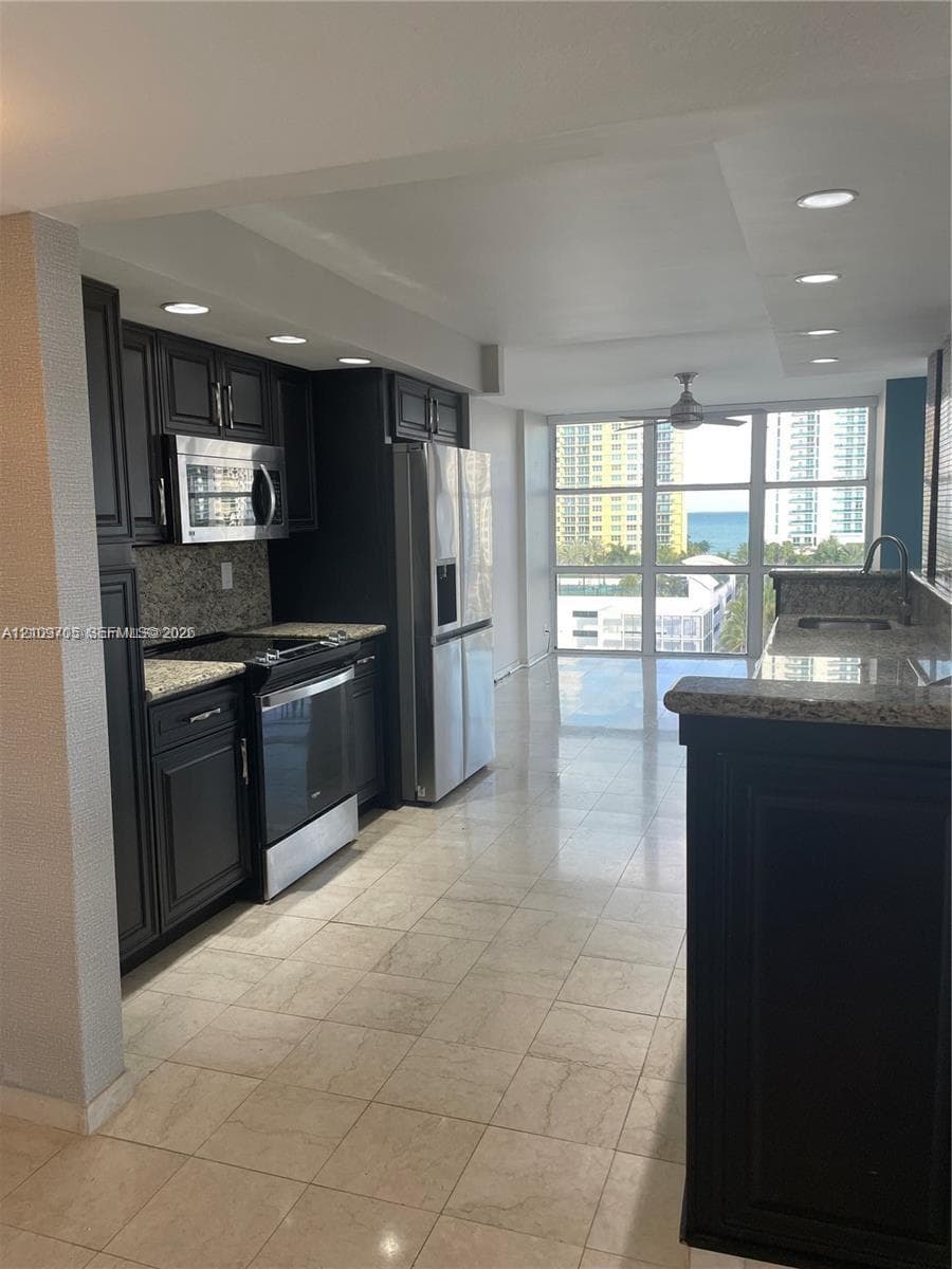 Kitchen featuring dark-finish cabinetry, stone-style countertops, stainless steel appliances, floor-to-ceiling windows, and tile flooring