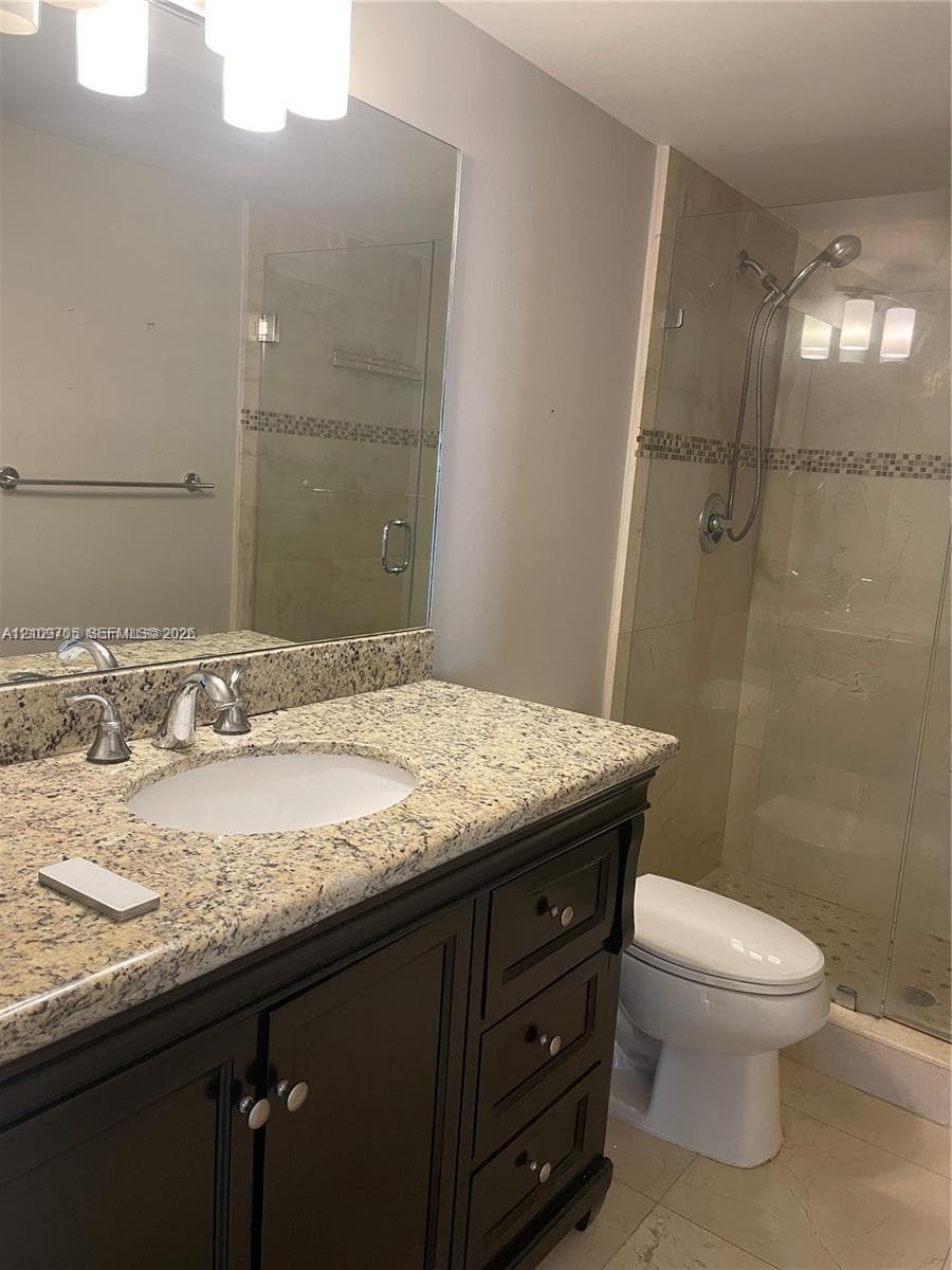 Bathroom featuring a dark wood-finish vanity with a stone countertop, an integrated sink, a glass-enclosed shower, and a large wall-mounted mirror