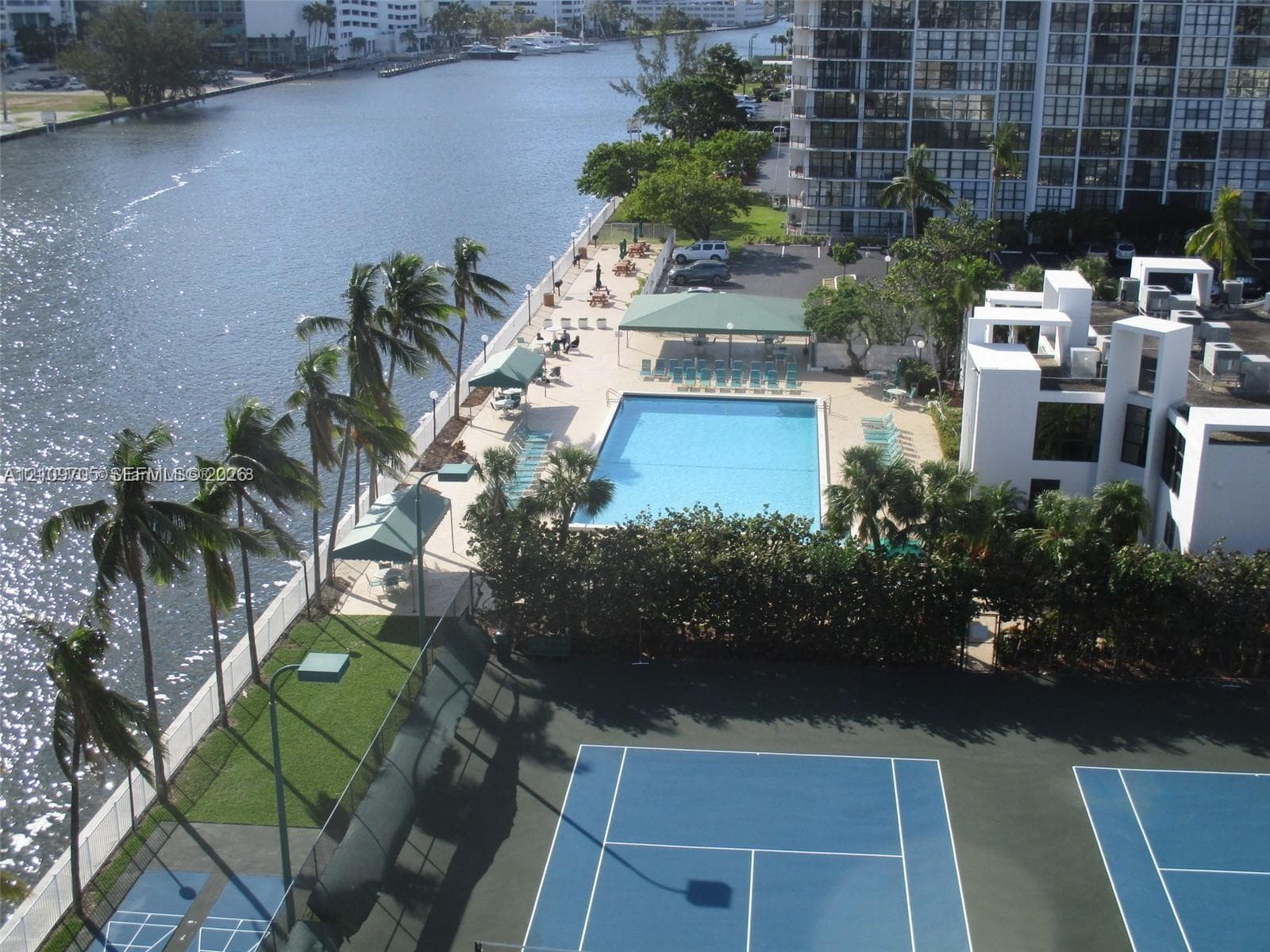 Waterfront property featuring a tennis court, swimming pool, paved sundeck, and palm tree landscaping