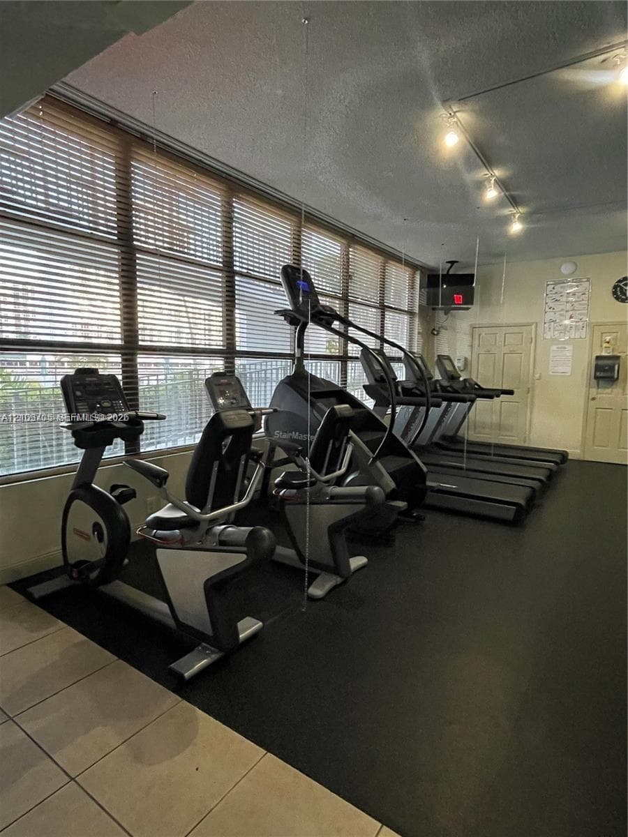 Fitness center featuring floor-to-ceiling windows, horizontal blinds, track lighting, and a combination of rubberized and ceramic tile flooring