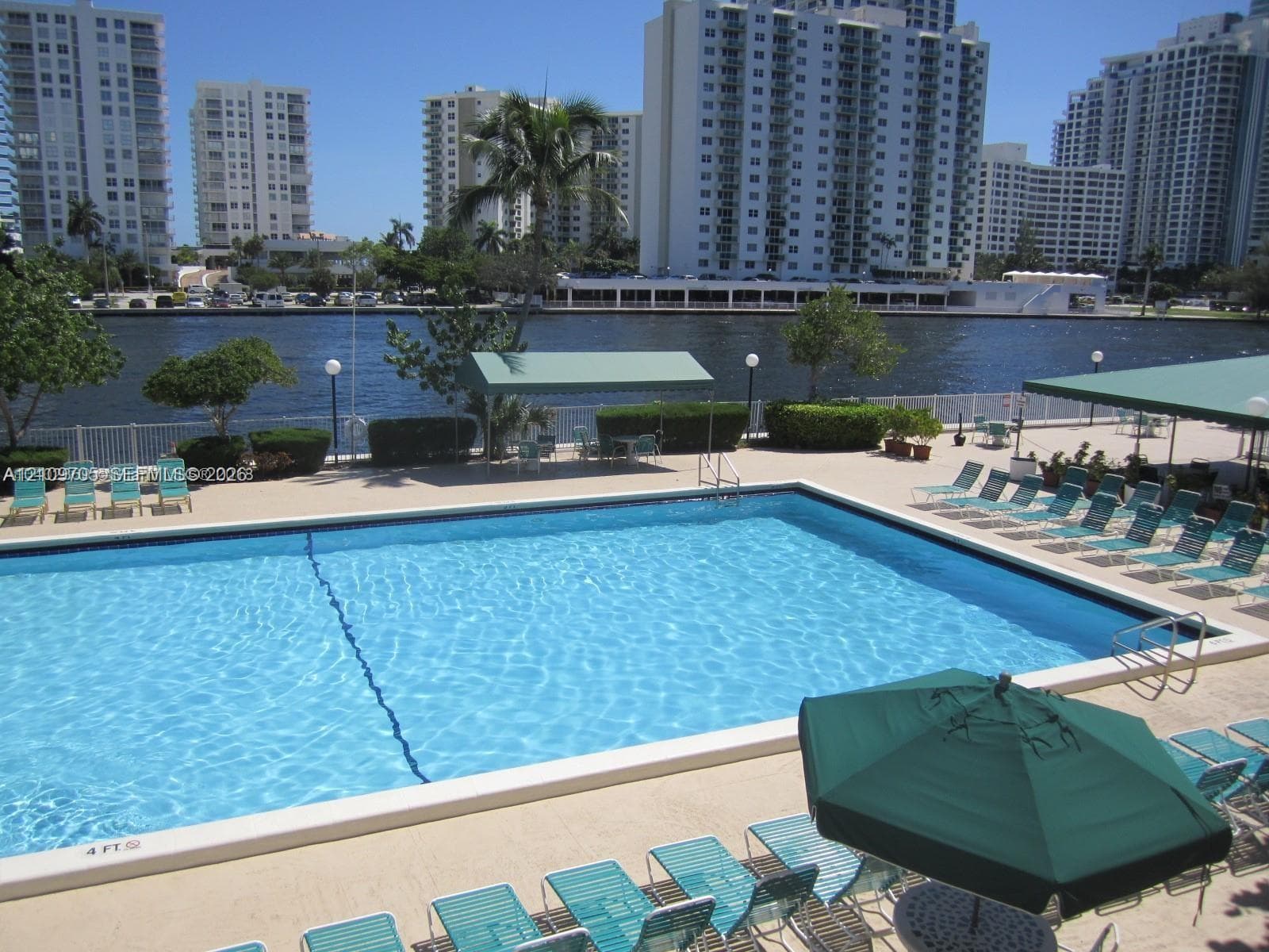 Waterfront swimming pool featuring a concrete deck, built-in lap lane, metal pool ladder, and shaded cabana structures