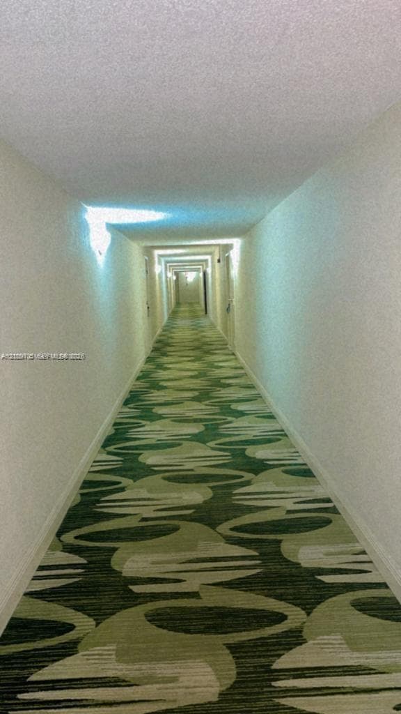 Interior corridor featuring patterned wall-to-wall carpeting and wall-mounted light fixtures