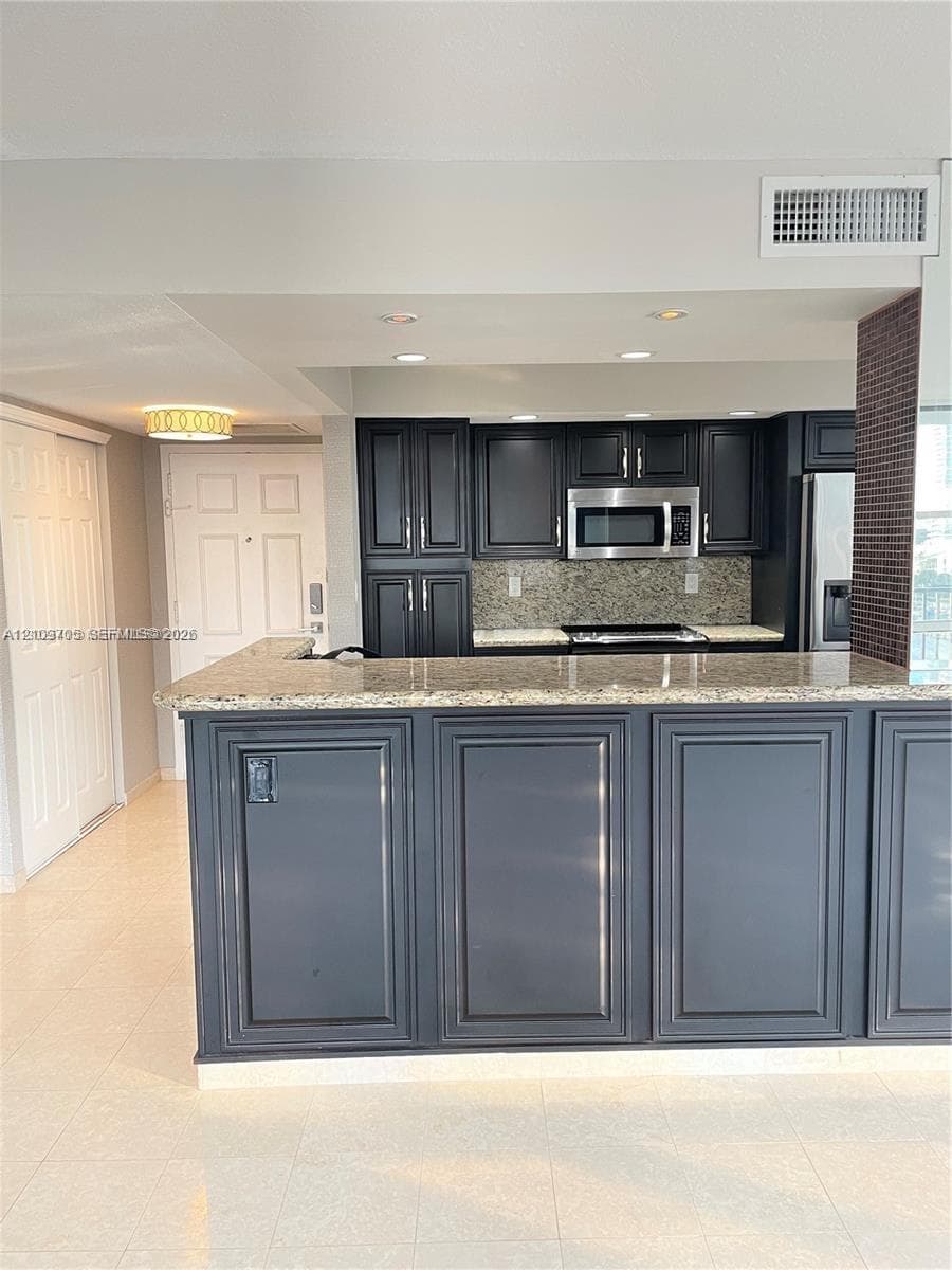 Kitchen featuring dark cabinetry, stone countertops, breakfast bar, recessed lighting, and stainless steel built-in microwave