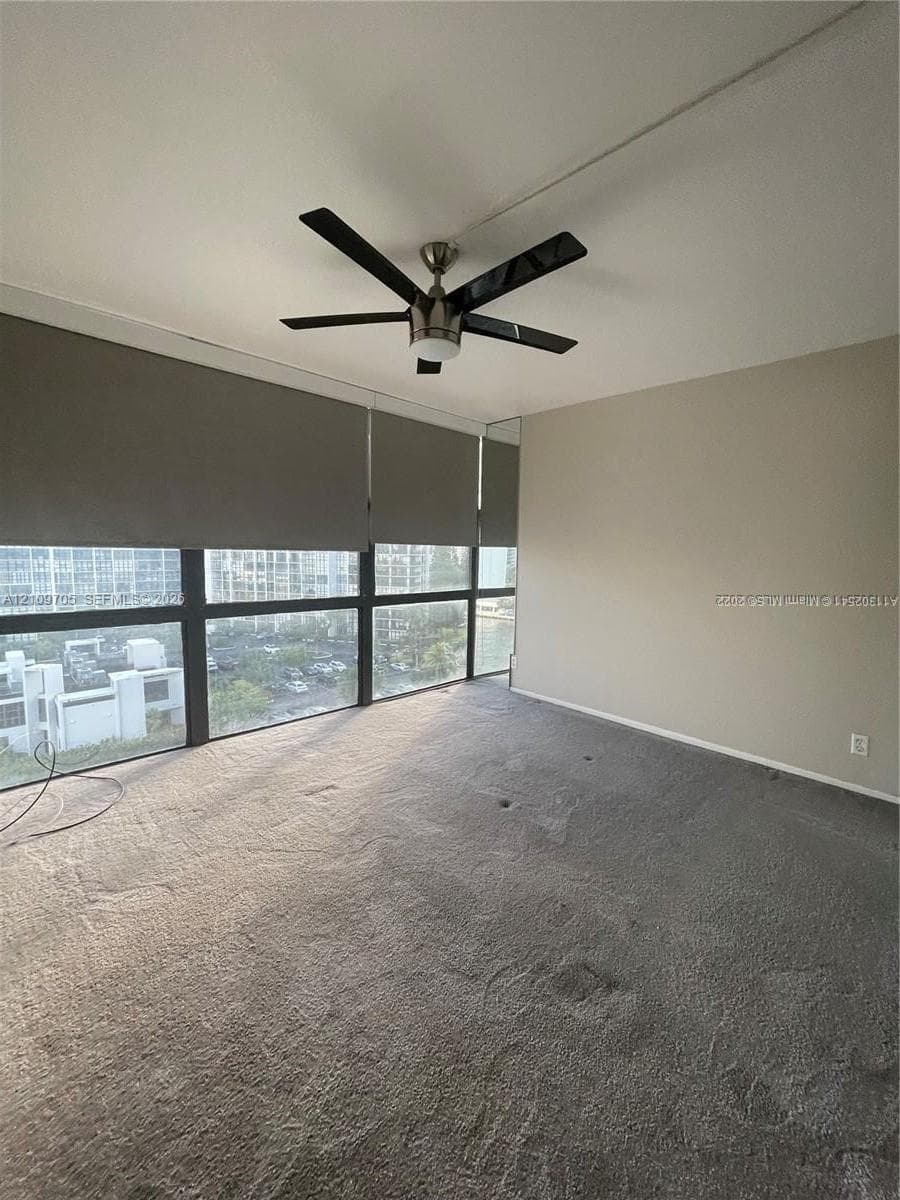 Interior space featuring floor-to-ceiling windows with black metal framing, a textured ceiling, neutral wall tones, and a six-blade ceiling fan with a metallic finish