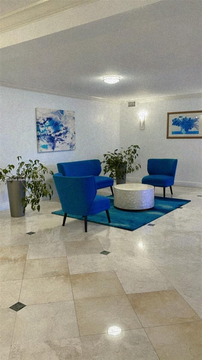 Polished stone flooring with decorative inset accents, crown molding, and wall-mounted lighting fixtures