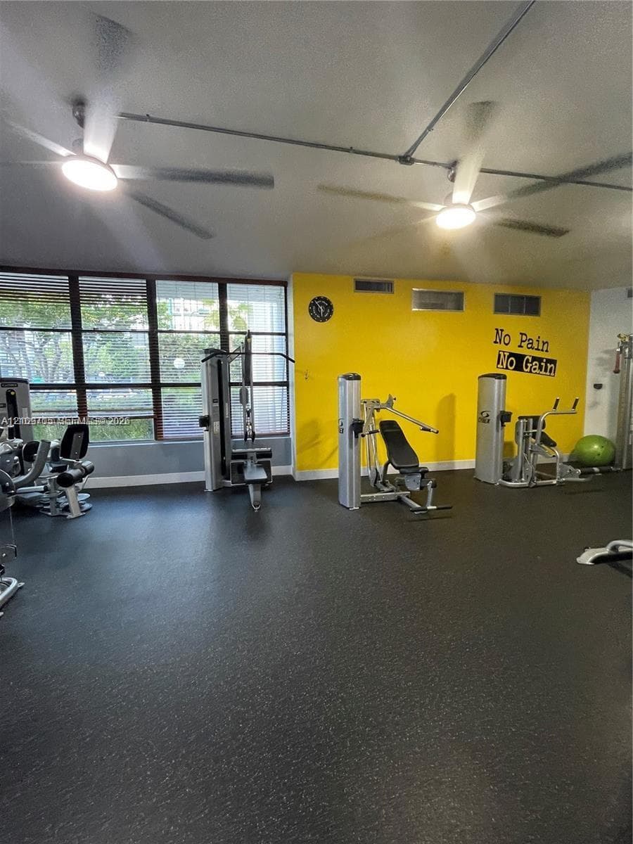 Fitness center featuring large floor-to-ceiling windows, durable rubberized flooring, and dual industrial-style ceiling fans with integrated lighting