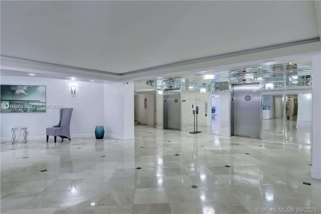 Lobby area featuring polished stone tile flooring with decorative inlay, stainless steel elevator doors, and mirrored wall paneling